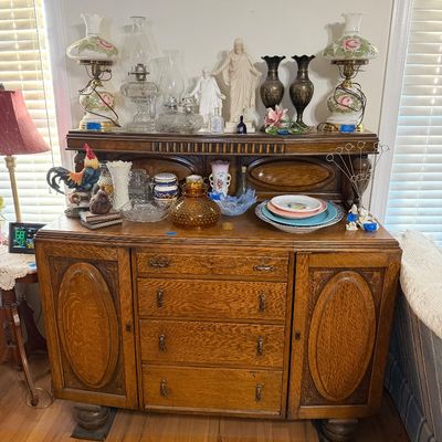 Antique quarter-sawn oak sideboard buffet with hutch top, featuring an array of vintage decor including painted oil lamps, glassware,...