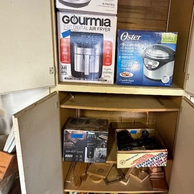 Tall storage cabinet filled with boxed kitchen appliances including an Instant Pot, Gourmia air fryer, and Oster roaster, alongside...