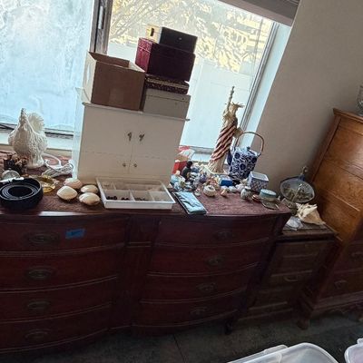 A wide mahogany double dresser topped with various collectibles, jewelry boxes, and decor, alongside a tall wooden chest of drawers.