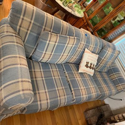 Plaid fabric sofa in shades of blue, cream, and brown, featuring rolled arms, matching throw pillows, and a traditional skirted base.
