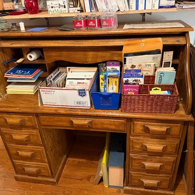 Traditional wooden roll-top desk with multiple storage drawers and cubbies, filled with various stationery and office supplies.