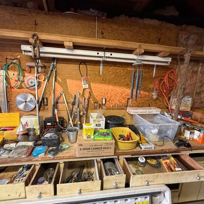 Workshop workbench filled with various hand tools, hardware, extension cords, and camping supplies.