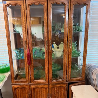 Traditional oak display cabinet with glass-front upper doors and carved details, filled with green depression glass and uranium glassware.