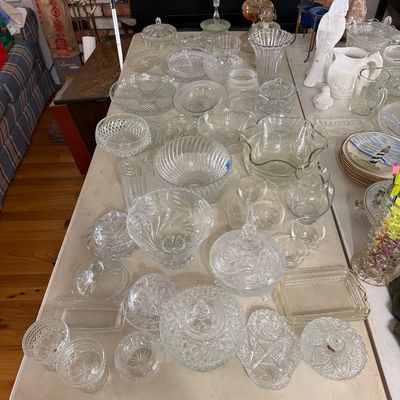 Large collection of vintage pressed, cut, and molded glassware displayed on folding tables, including covered candy dishes, serving...