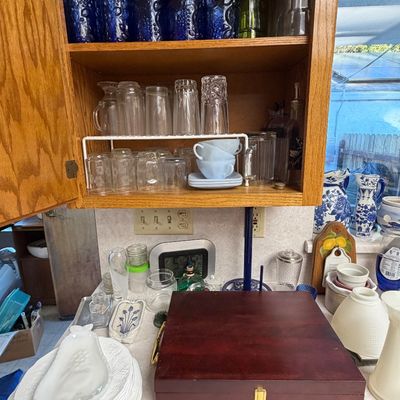 A wooden cabinet filled with cobalt blue and clear glassware sits above a kitchen counter displaying a mahogany silverware chest, milk...