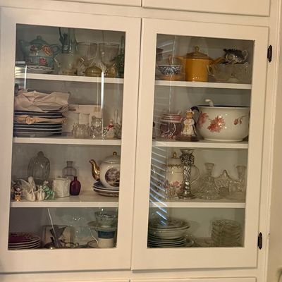 White built-in display cabinet filled with an assortment of vintage glassware, teapots, porcelain figurines, and dinnerware.
