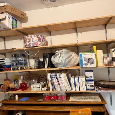 Wall-mounted utility shelves organized with various office supplies, photo paper, storage boxes, and household knick-knacks above a...