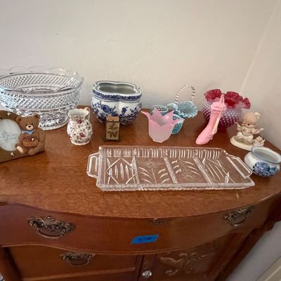 Collection of vintage decorative glassware, ceramics, and small collectibles arranged on a wooden dresser surface.