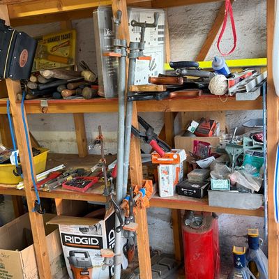 Wooden workshop shelving unit packed with various hand tools, pipe clamps, hardware supplies, and automotive equipment.