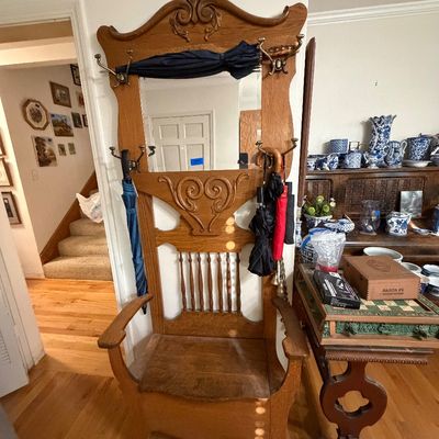 Antique carved oak hall tree featuring a central mirror, brass coat hooks, spindle backrest, and integrated bench seat.