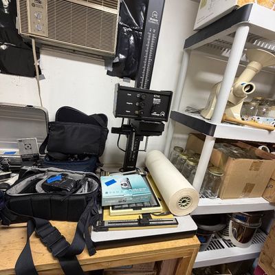 Omega C700 Modular System photo enlarger with Super Chromega C dichroic head, displayed alongside camera bags, photo paper, and various...