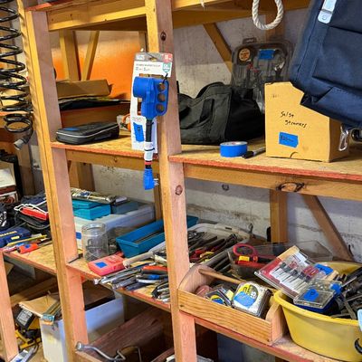 Workshop shelving unit organized with various hand tools, hardware, electrical adapters, and storage bags.