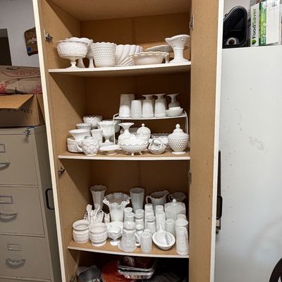 Tall white laminate storage cabinet filled with vintage milk glass tableware and kitchen accessories.