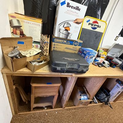 Workbench displaying various household items, boxed small appliances including a Breville Citrus Press and Oreck Air Purifier, a vintage...