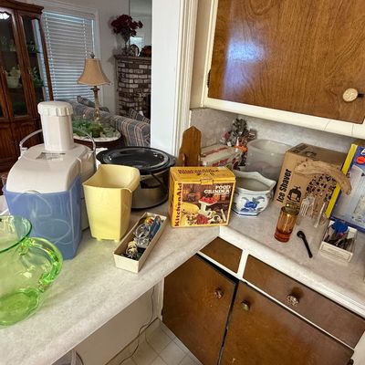 Kitchen countertop with various appliances and glassware, including a green glass pitcher, white juice extractor, slow cooker, and boxed...