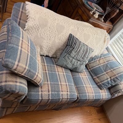 Blue and beige plaid upholstered loveseat, styled with a grey throw pillow and a cream crocheted blanket.