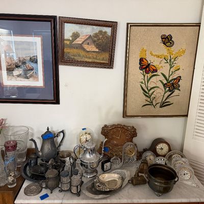 Collection of tabletop decor including silver-plated teapots, crystal glassware, and various vintage mantle clocks, displayed below...