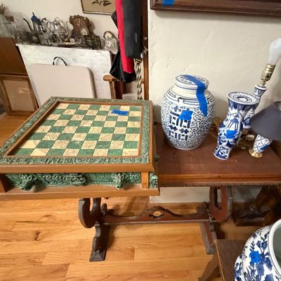 Ornate carved Aztec-style stone and wooden chessboard set on a wooden console table alongside various blue-and-white porcelain urns and...
