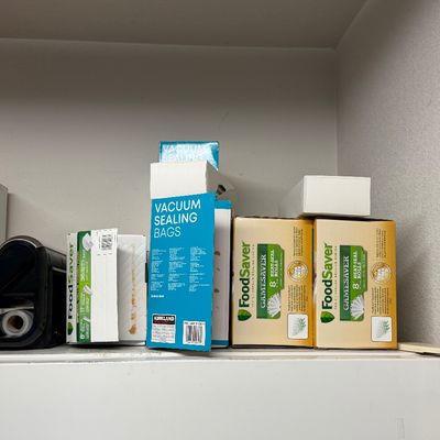 FoodSaver vacuum sealer machine alongside multiple boxes of FoodSaver and Kirkland brand vacuum sealing heat-seal rolls and bags.