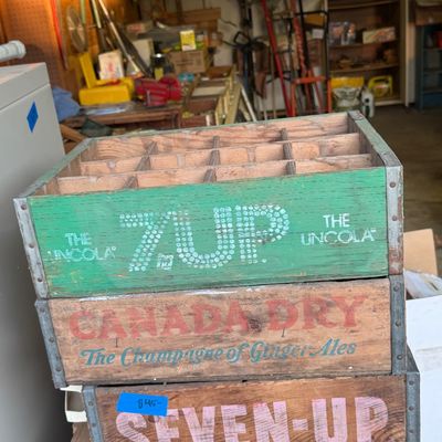 Stack of three vintage wooden soda crates with metal corner reinforcements, including green and natural wood 7-Up and Canada Dry crates.