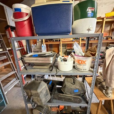 Four-tier metal shelving unit holding vintage Coleman coolers, electric buffet servers, power tool cases, and extension cord spools.
