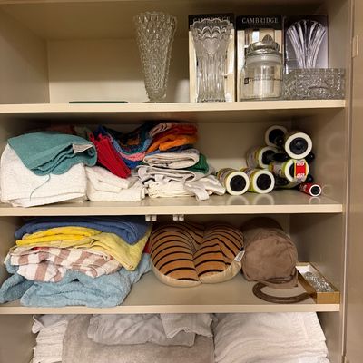 Linen cabinet filled with assorted bath towels, washcloths, travel pillows, lint rollers, and crystal vases.
