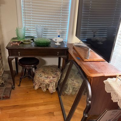 A wooden writing desk displaying colorful depression glass pieces alongside a flat-screen television on a console table, complemented by...