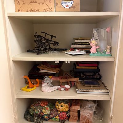 Cabinet shelves filled with assorted decor, including Jim Shore boxes, Precious Moments figurines, picture frames, and a patchwork cat...