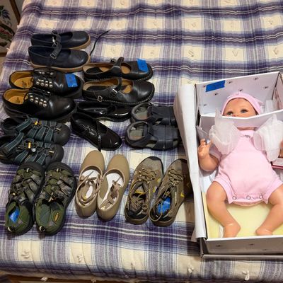 Collection of children's and women's footwear alongside a realistic lifelike baby doll in its original box.
