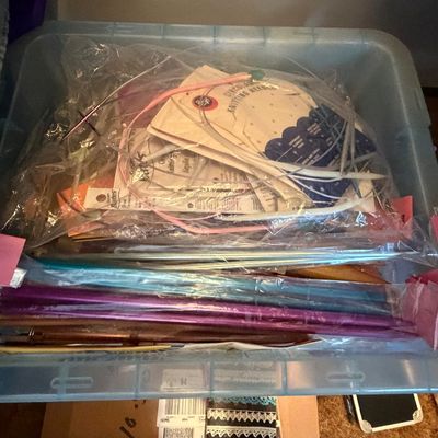 Plastic storage tote filled with assorted knitting supplies, including straight and circular knitting needles in various sizes.