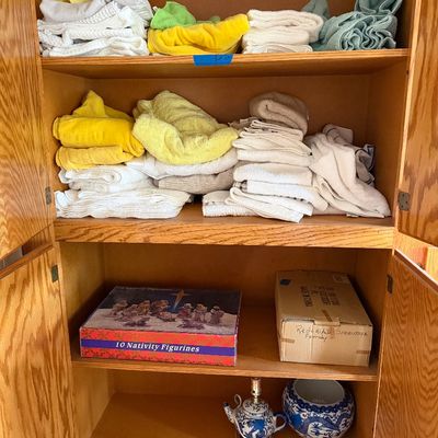 Sale Photo Thumbnail #103: Wooden linen cabinet filled with folded towels, boxed holiday decorations including a 10-piece nativity set, and blue-and-white porcelain items.