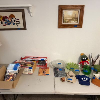 Assorted estate items on a folding table, including a boxed Team Associated RC10 buggy, comic books, glassware, baseball caps, and framed...