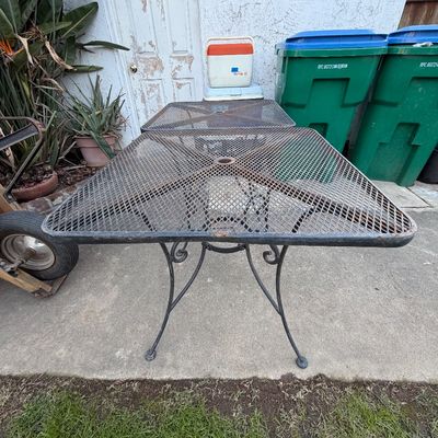 Vintage black wrought iron patio table with a square mesh top and central umbrella hole, showing light surface rust.