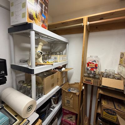 A collection of home canning supplies, including boxed Mason jars, a steam juicer, a food strainer, and storage shelves.