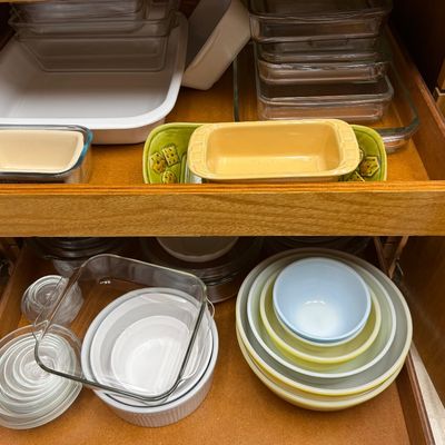 Wooden cabinet shelves filled with assortment of vintage bakeware, glass storage dishes, ceramic loaf pans, and Pyrex nesting bowls.