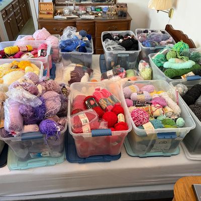 Large collection of assorted yarn skeins and balls sorted by color, organized inside clear plastic storage bins.