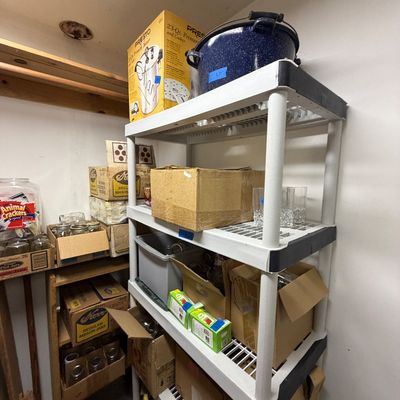 White plastic shelving unit holding various canning supplies, including a boxed Presto pressure cooker, blue speckled roaster pan, and...