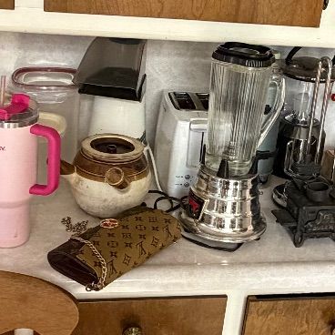 Collection of kitchen items including a pink Stanley tumbler, chrome blender, vintage ceramic crocks, and a flat of small glass jars on a...