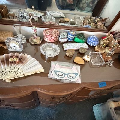 Collection of vintage vanity items displayed on a wooden dresser, including a decorative hand fan, trinket boxes, a small desk clock, and...