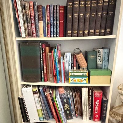 Tall white wooden bookcase filled with various hardcovers, paperbacks, book sets, and small decorative boxes.