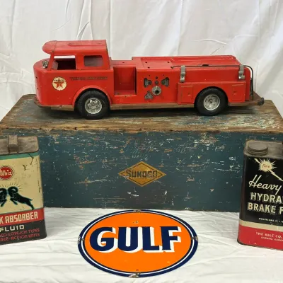 Vintage automobilia collectibles including a red Texaco Fire Chief toy truck, two vintage oil and fluid cans, and an oval Gulf porcelain...