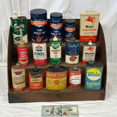 Collection of vintage mid-century petroliana and household oil cans displayed on a wooden tier shelf, including brands such as Mobil,...