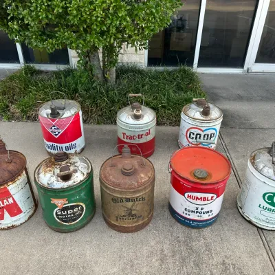 Collection of eight vintage 5-gallon metal oil cans featuring brands like Macmillan, Conoco, Humble, Old Dutch, Skelly, and Co-op with...