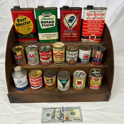 Collection of vintage automotive fluid cans and coin banks displayed on a three-tier wooden shelf, including brands like Rust Master,...