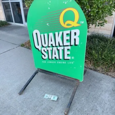 Vintage double-sided Quaker State metal sidewalk sign on a painted metal frame, showing light surface scuffs and wear.