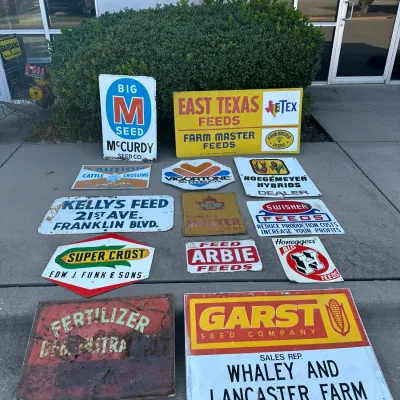 Collection of vintage agricultural and feed metal advertising signs, featuring brands like Garst Seed Company, East Texas Feeds, and Big...