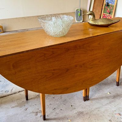 Mid-century modern wooden drop-leaf dining table with tapered legs, topped with a cut glass bowl and a brass duck figurine.