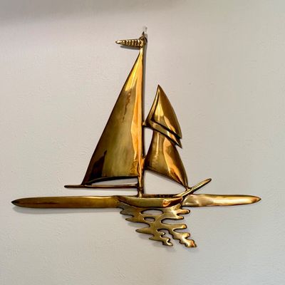 Vintage mid-century brass sailboat wall art sculpture, featuring stylized sails and water reflection details.