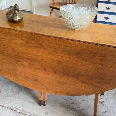 Mid-century modern walnut drop-leaf console table with tapered legs, topped with a brass duck figurine and a crystal bowl.