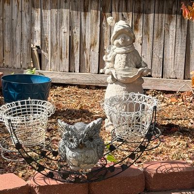 Collection of outdoor garden decor including concrete owl and snowman statues alongside wire plant holders and a blue planter.